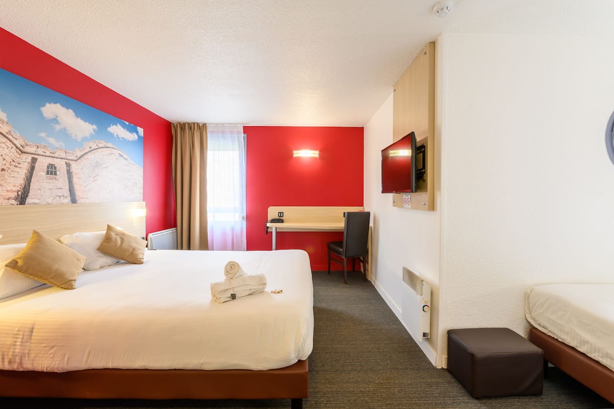 Habitación de hotel con una cama grande, un escritorio, una silla, un televisor y un taburete pequeño.