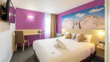 A hotel room with a bed, a desk, a chair, a TV, and a painting on the wall.