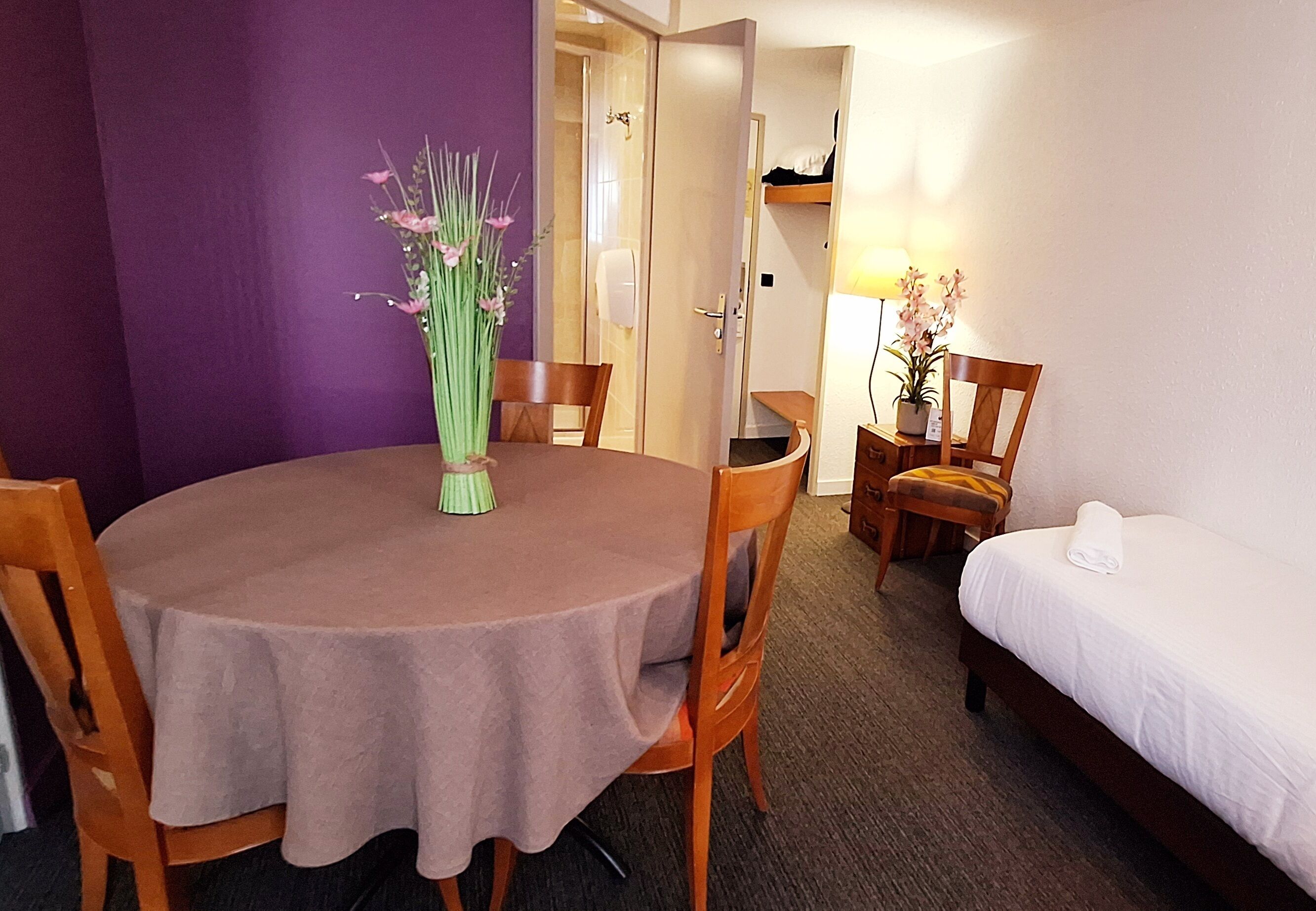 Une chambre d’hôtel avec une table de salle à manger ronde, un lit simple et une chaise.