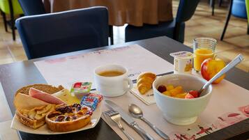A breakfast setting with toast, ham, cheese, croissant, coffee, fruit bowl, and juice on a table.