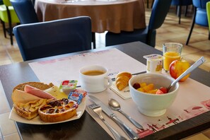 Una mesa con desayuno que incluye tostadas, jamón, queso, croissant, café, frutero y jugo.