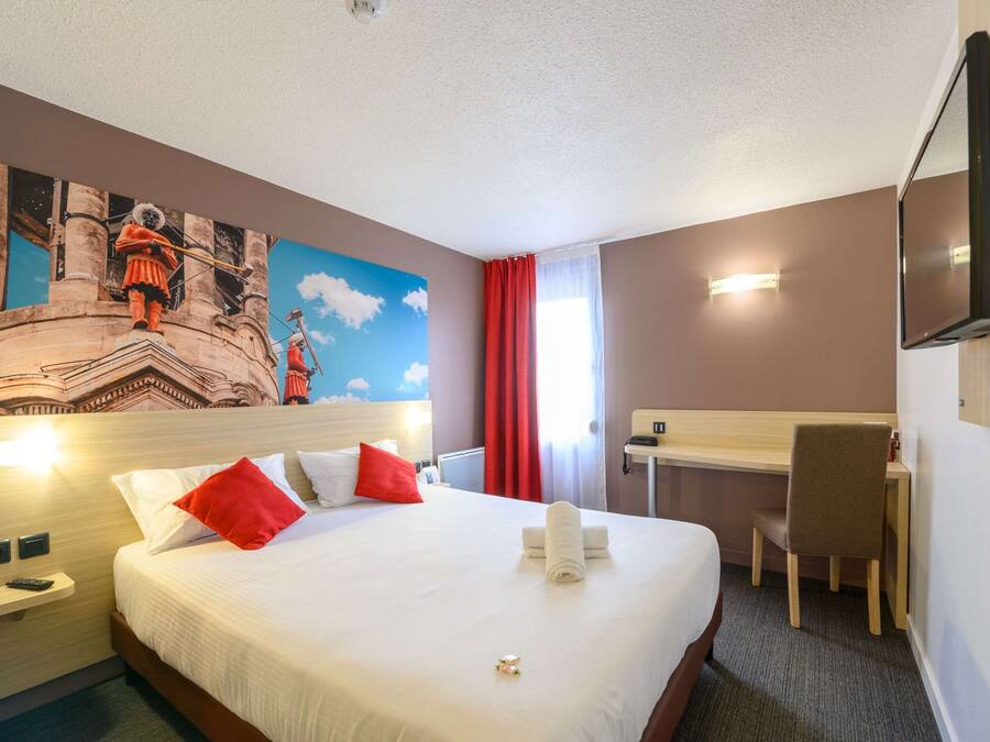 A hotel room with a bed, a desk, a chair, a TV, and a mural on the wall.