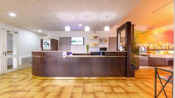 A hotel reception area with a wooden reception desk, a digital display, and a wall-mounted TV.