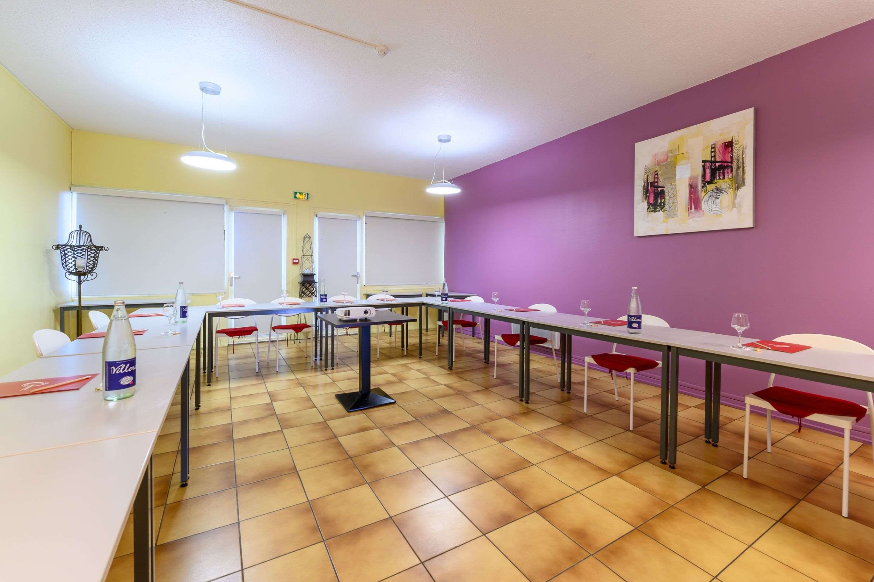 Une salle de conférence équipée de plusieurs tables et chaises, d’un projecteur et d’une bouteille d’eau posée sur une table.