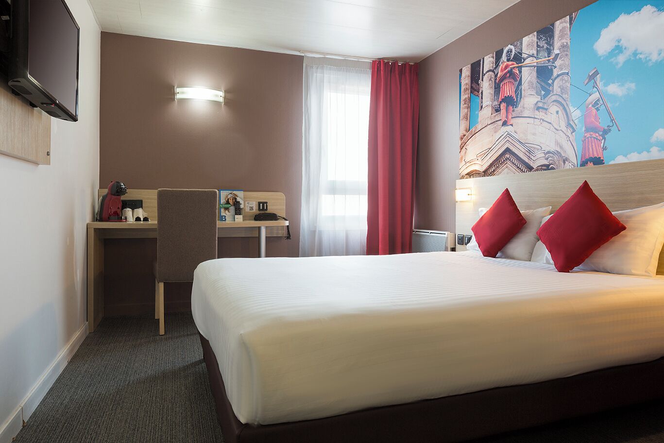 A hotel room with a bed, a desk, a chair, a TV, and a painting on the wall.