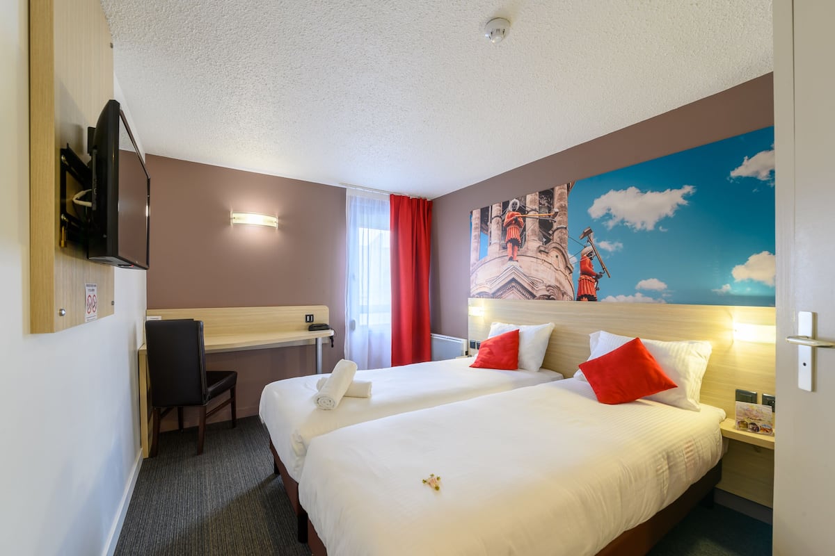 Una habitación de hotel con dos camas, un escritorio, una silla, un televisor y un mural en la pared.