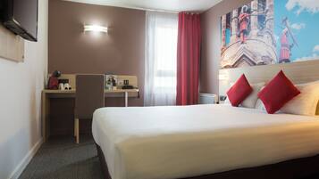 Habitación de hotel con cama, escritorio y silla. Hay un cuadro en la pared y una ventana con cortinas.