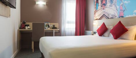 A hotel room with a bed, a desk, and a chair. There is a painting on the wall and a window with curtains.