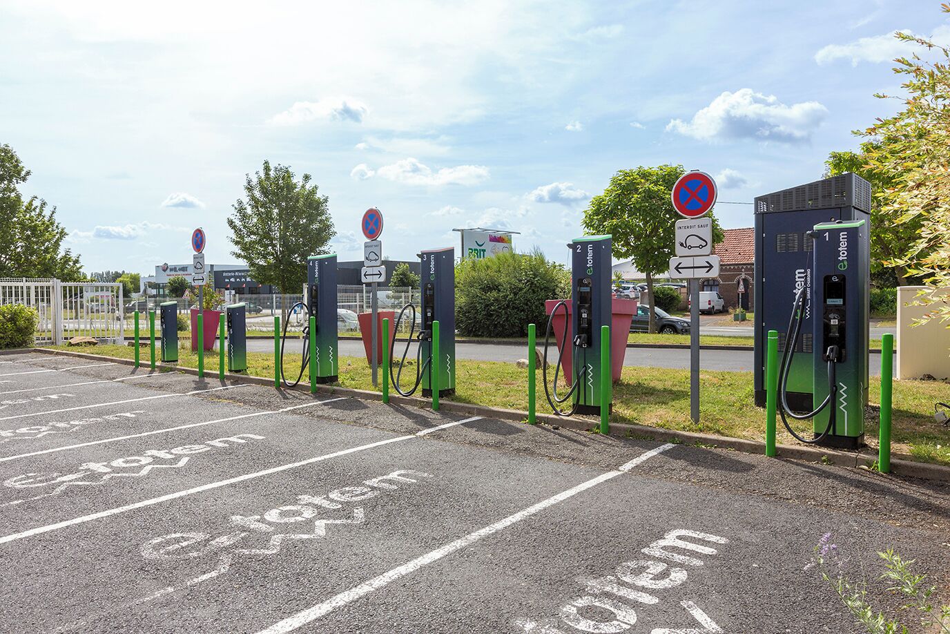 Un estacionamiento con estaciones de carga para vehículos eléctricos, espacios delimitados y un letrero de prohibido estacionar.