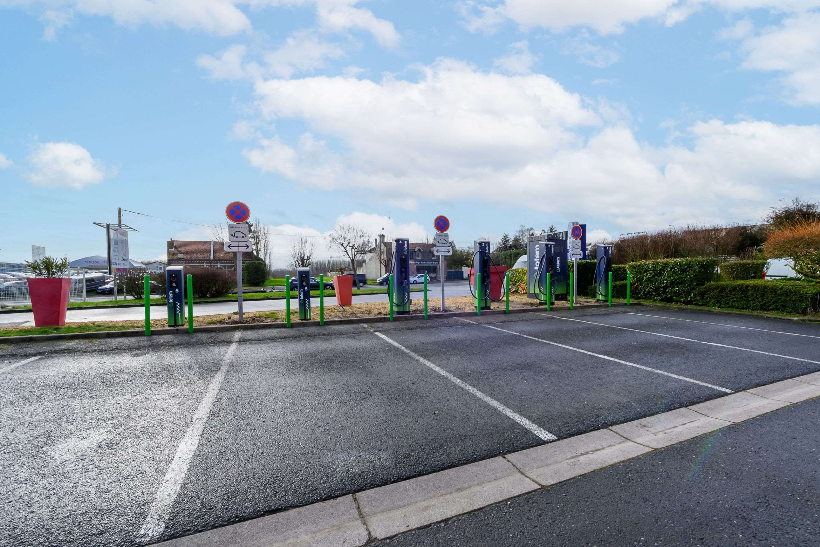 Un área de estacionamiento con varias estaciones de carga para vehículos eléctricos, un letrero de prohibido estacionar y una señal de orientación.