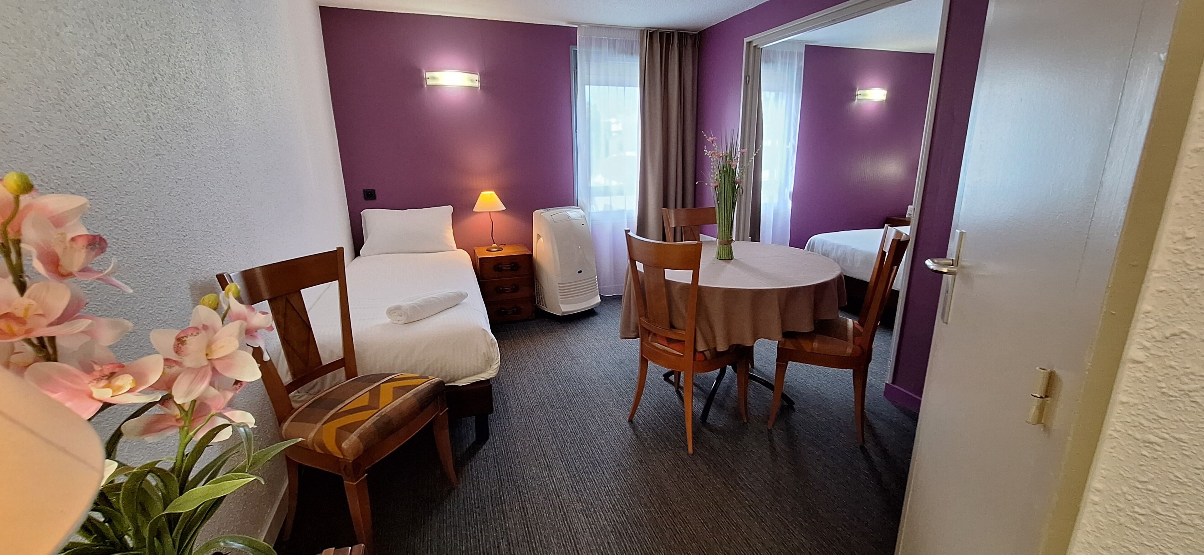 Une chambre d’hôtel comprenant un lit, un bureau, une chaise, une table, une lampe et une plante en pot.