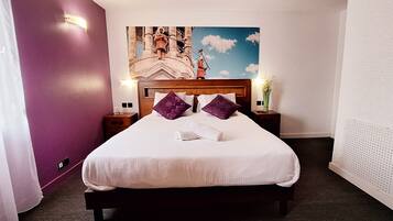 Una habitación de hotel con cama, almohadones morados, una mesita de noche, una lámpara de pared y un adorno mural.