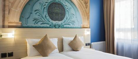 Ein Hotelzimmer mit einem großen Bett, zwei Nachttischen, einer Zierbogenwand und einem Fenster mit Vorhängen.