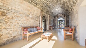 Interior con paredes de piedra, un banco de madera, una mesa de centro y una zona de comedor con sillas.