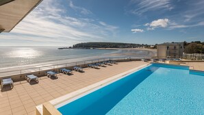 Una piscina con sillas de descanso y vistas a la playa y el océano.