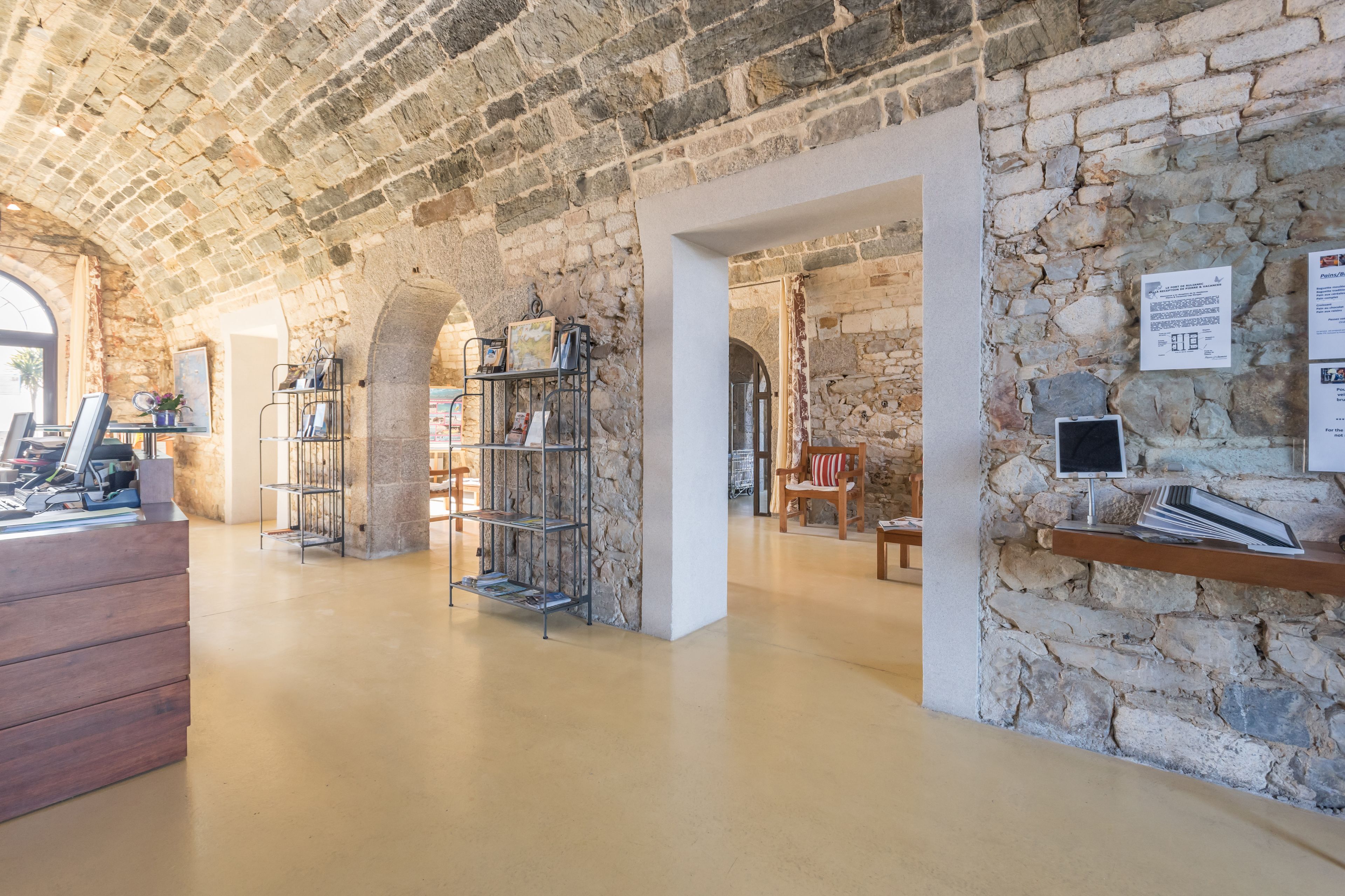 A stone-walled interior with a wooden desk, shelves, and a chair.