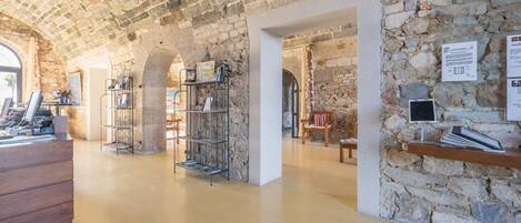 A stone-walled interior with a wooden desk, shelves, and a chair.