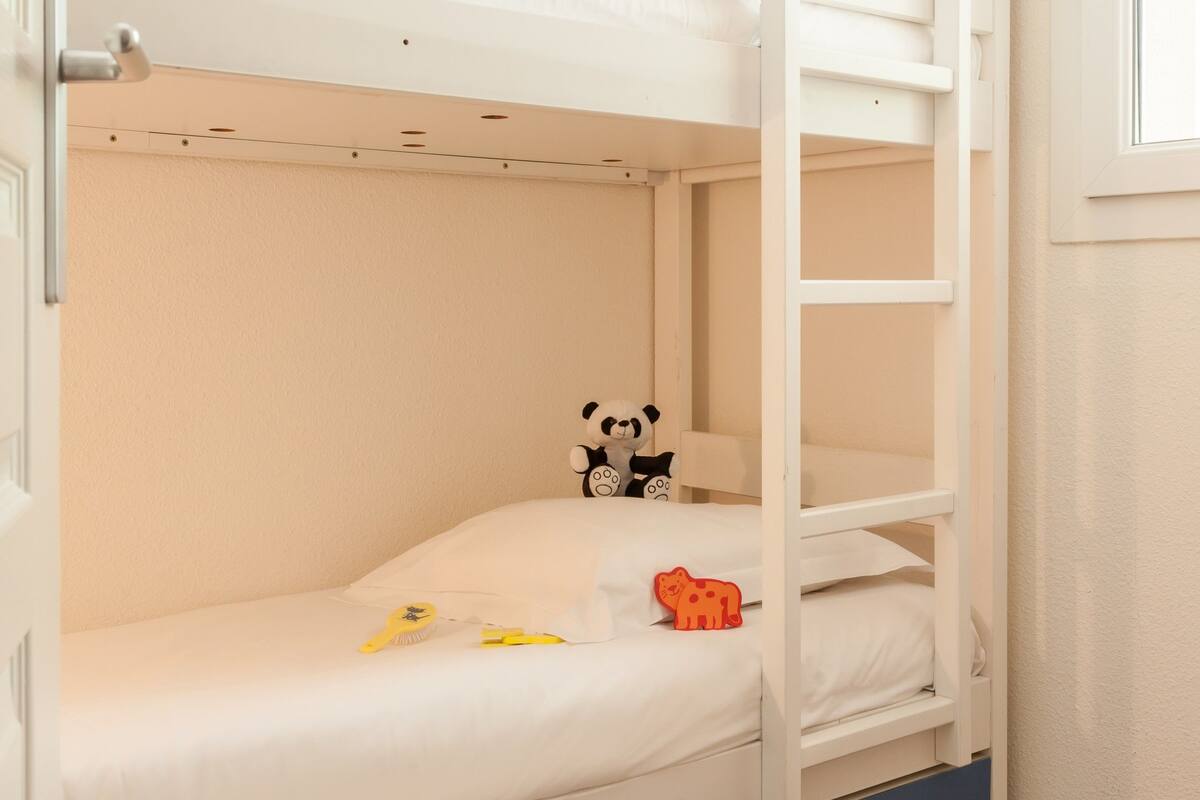 Una cama litera con escalera, un peluche de panda y un coche de juguete en la cama inferior.