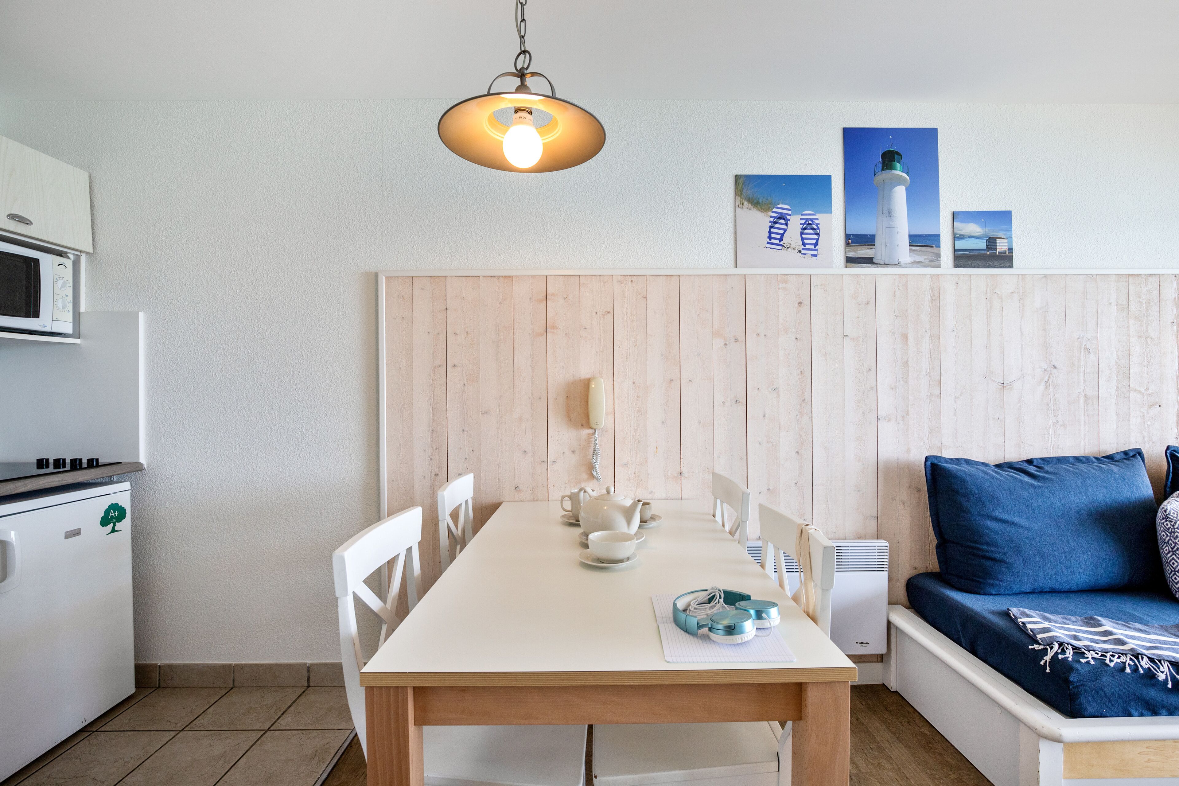 Een kleine keuken met een magnetron, fornuis en witte kastjes. Een eettafel met stoelen staat in het midden.