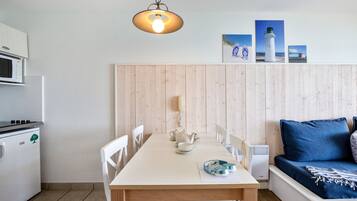 A compact kitchen with a microwave, stove, and white cabinets. A dining table with chairs is set up in the center.