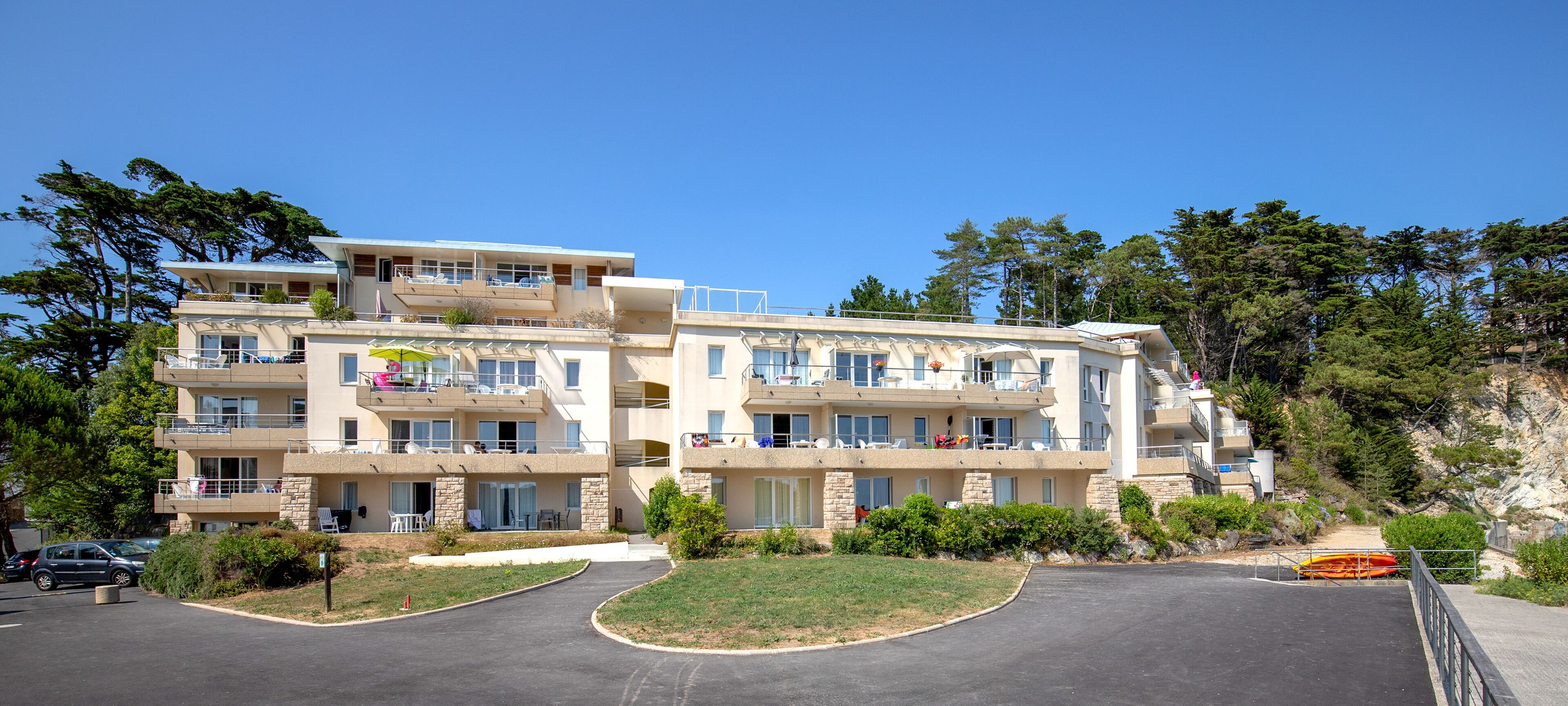 A multi-story hotel with balconies, a parking area, and a pathway leading to the entrance.