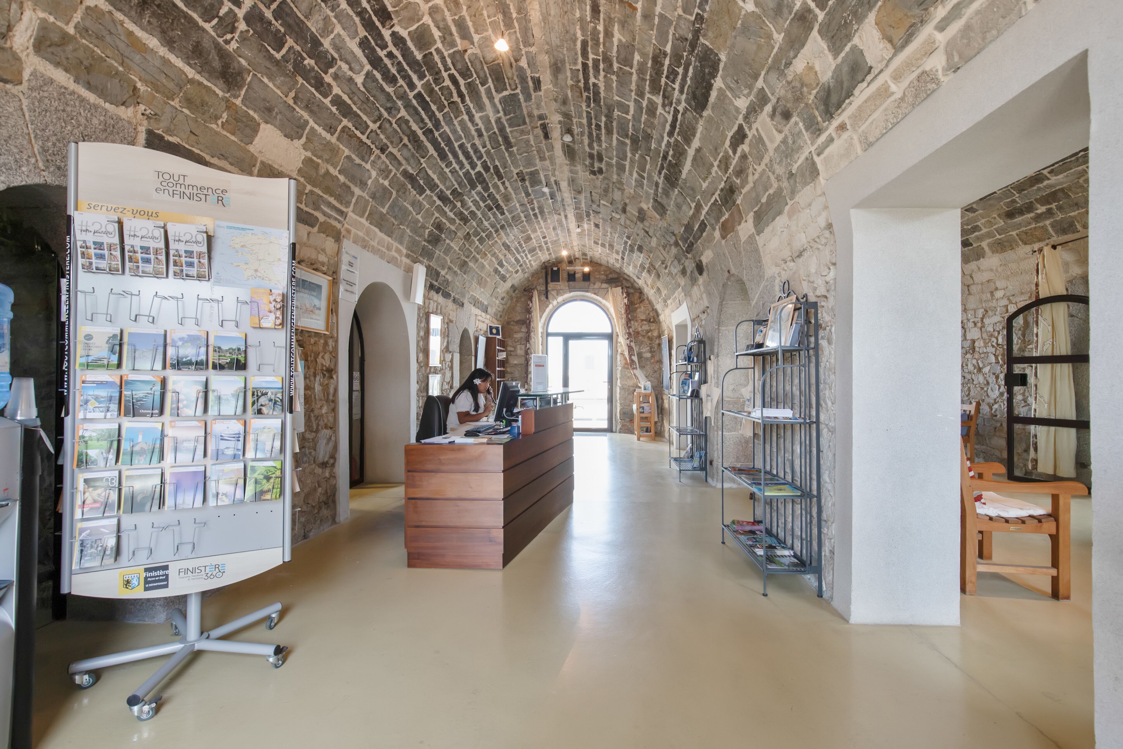 A spacious lobby with a high arched brick ceiling, a reception desk, and a display of postcards.