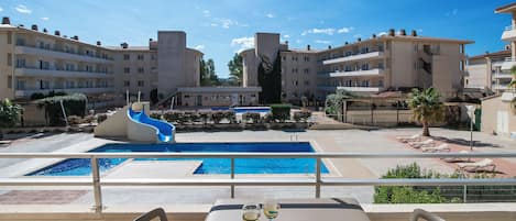 A hotel pool area with a slide, lounge chairs, and a table with a plate of grapes and two glasses of wine.