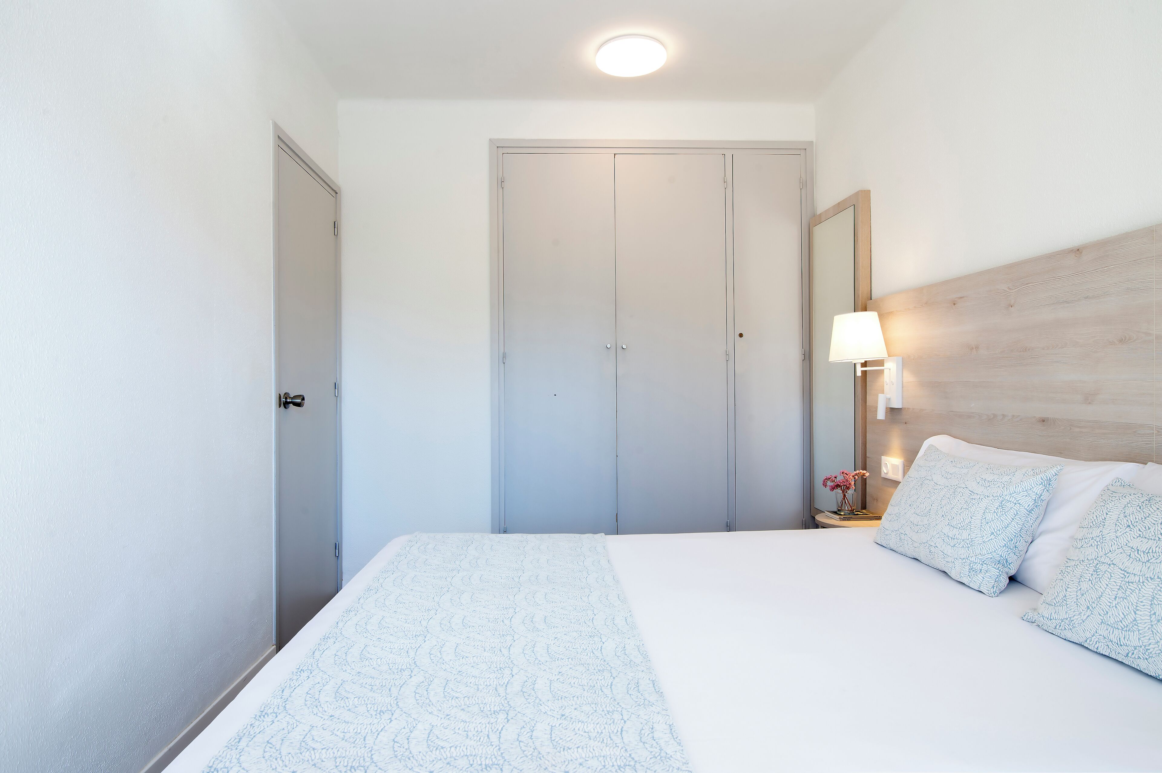 A hotel room with a bed, a nightstand with a lamp, and a wardrobe.