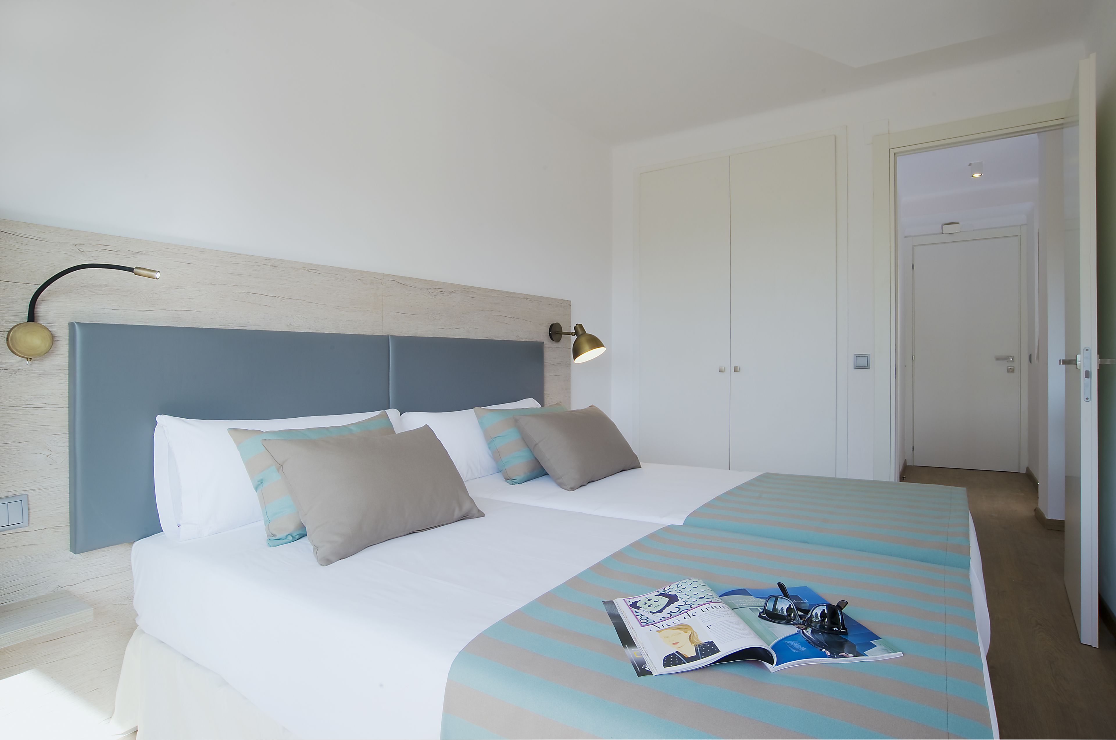 A neatly made bed with a striped bedspread, a bedside lamp, and a magazine on the bed.
