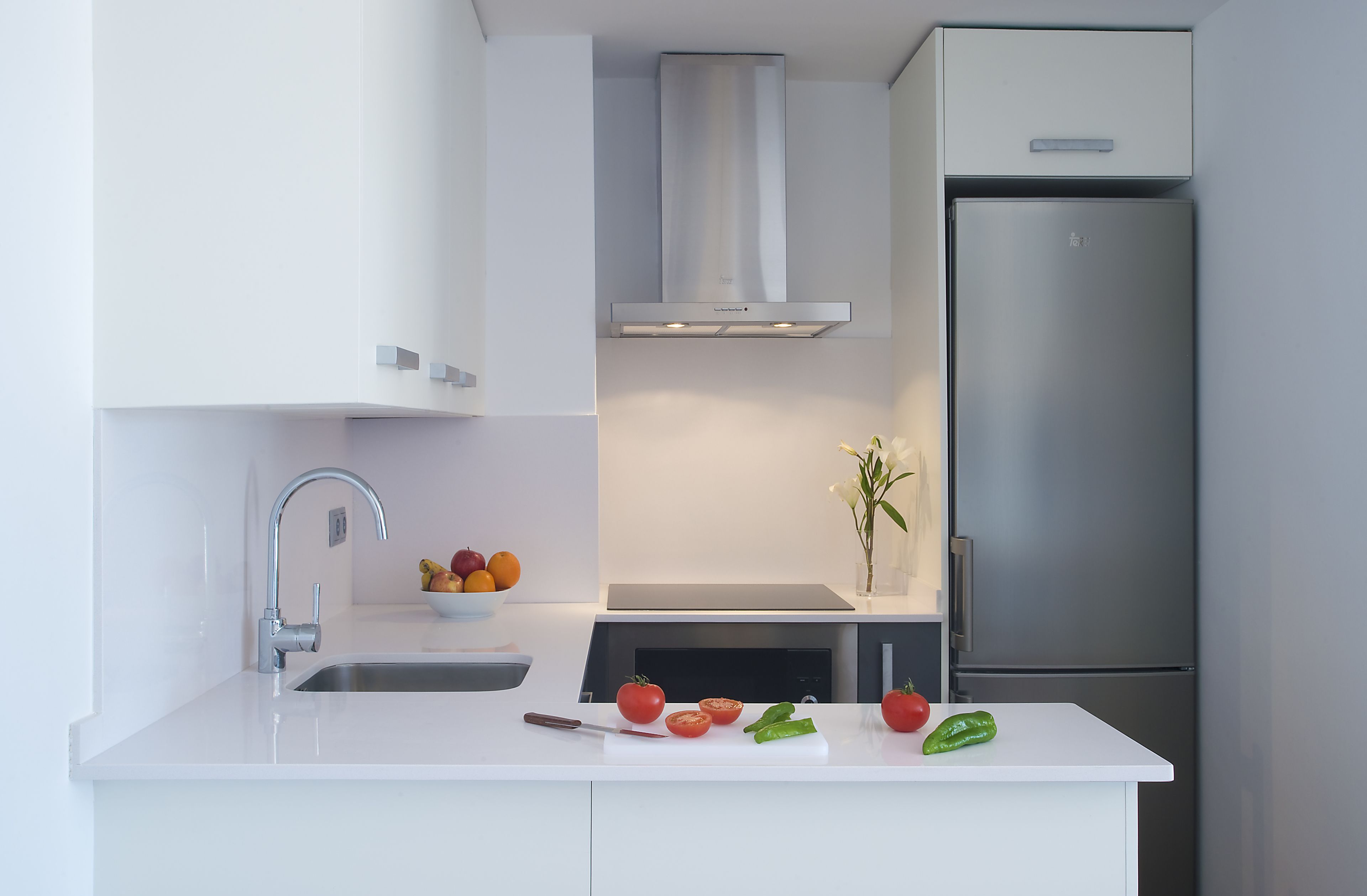 Una cocina moderna con un refrigerador de acero inoxidable, un horno empotrado y una encimera blanca.