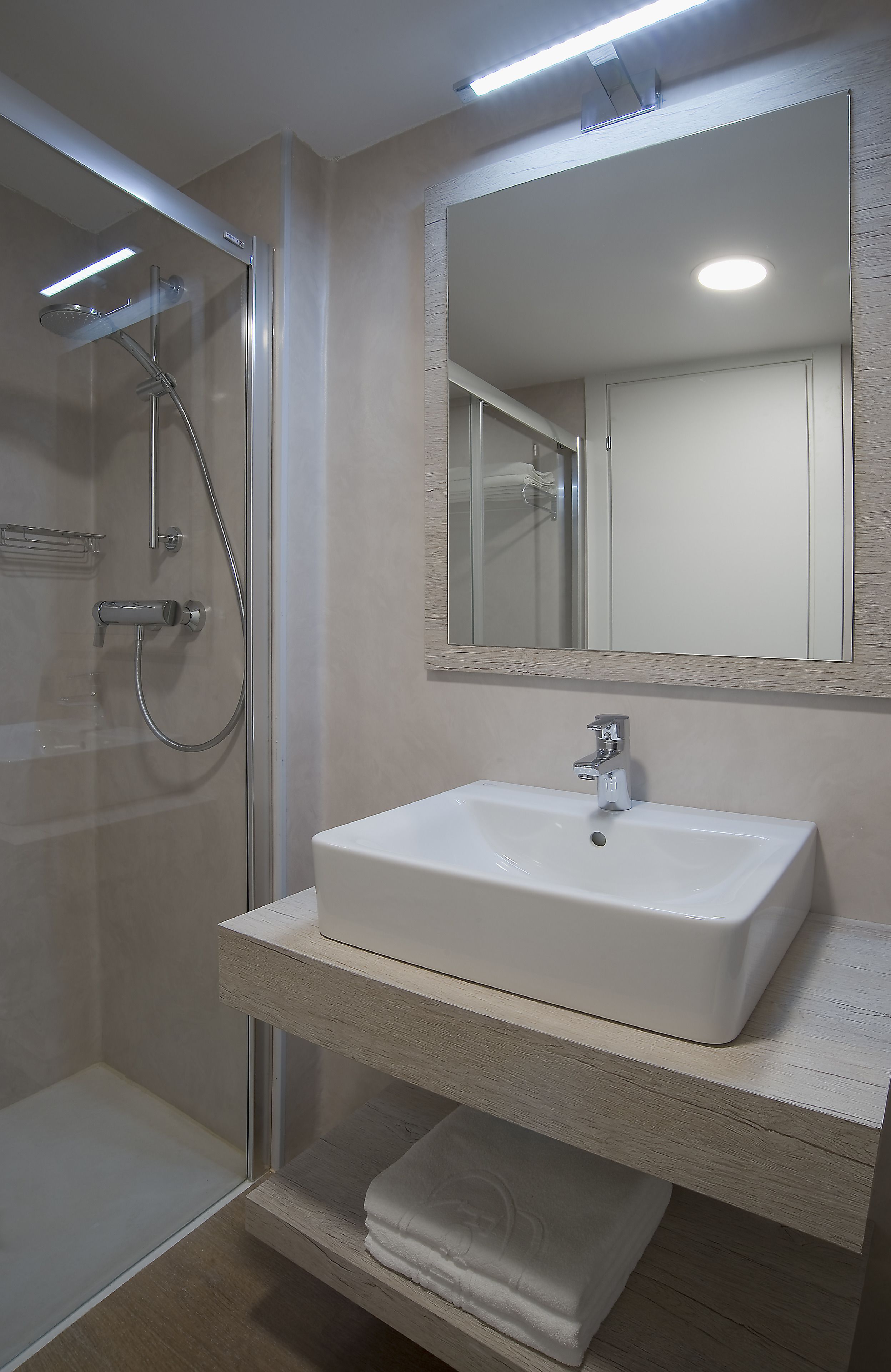 Ein modernes Badezimmer mit einer gläsernen Dusche, einem weißen Waschbecken und einem Spiegel darüber.