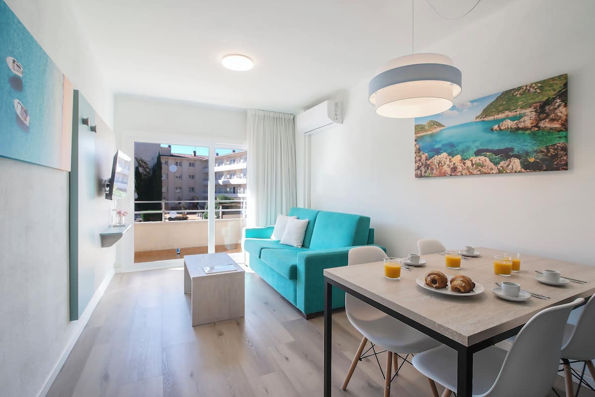 Een moderne hotelkamer met een zithoek, een blauwgroene bank en een schilderij van een kustlandschap.