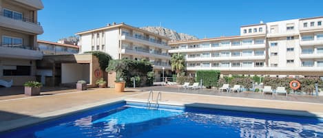 Une piscine à l’eau d’un bleu cristallin, entourée d’un bâtiment doté de nombreux balcons, avec une montagne en toile de fond.
