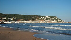 Une plage avec vue sur une ville côtière et un pont qui se dessine à l’horizon.