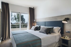 Une chambre d’hôtel avec un grand lit, deux tables de chevet, une commode, une fenêtre avec des rideaux et une vue sur les arbres à l’extérieur.
