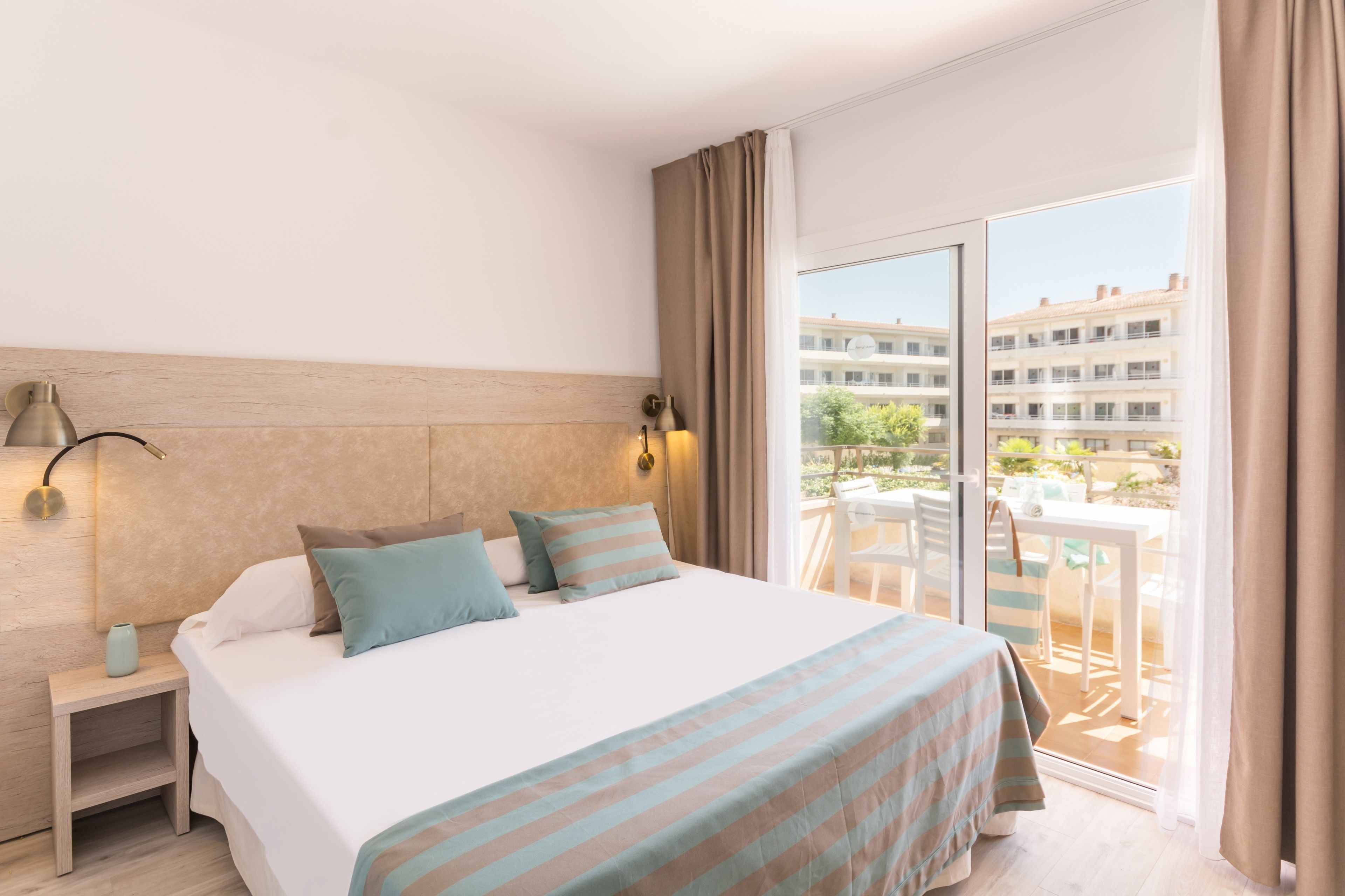 A hotel room with a bed, bedside tables, a lamp, and a view of the outside balcony.