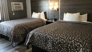 Habitación de hotel con dos camas, cabecero de madera oscura, mesita de noche con lámpara y unidad de aire acondicionado.