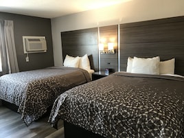 Habitación de hotel con dos camas, cabecero de madera oscura, mesita de noche con lámpara y unidad de aire acondicionado.