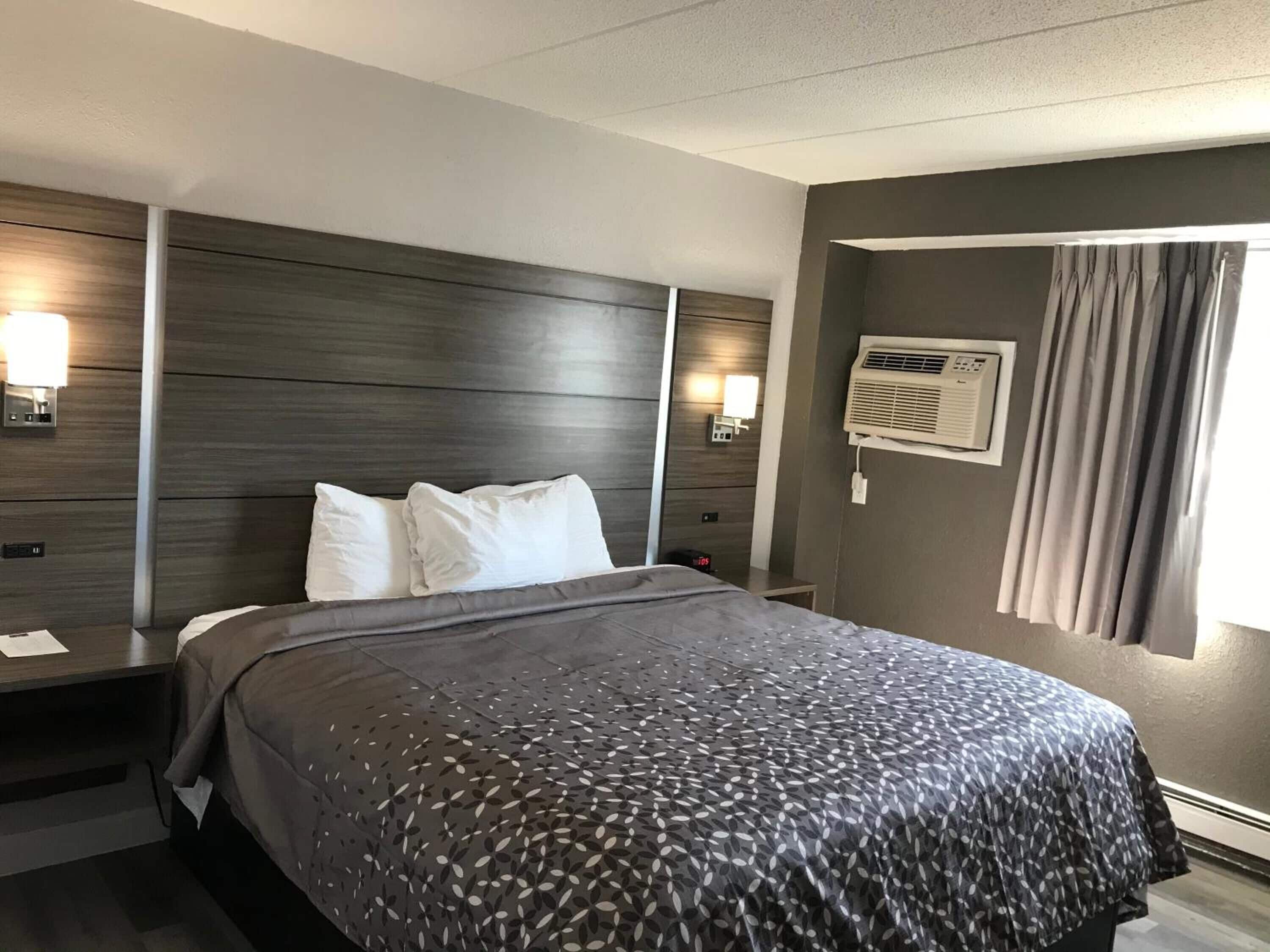 Una habitación de hotel moderna con una cama grande, cabecera de madera oscura, lámparas de noche y un ventanal con cortinas.