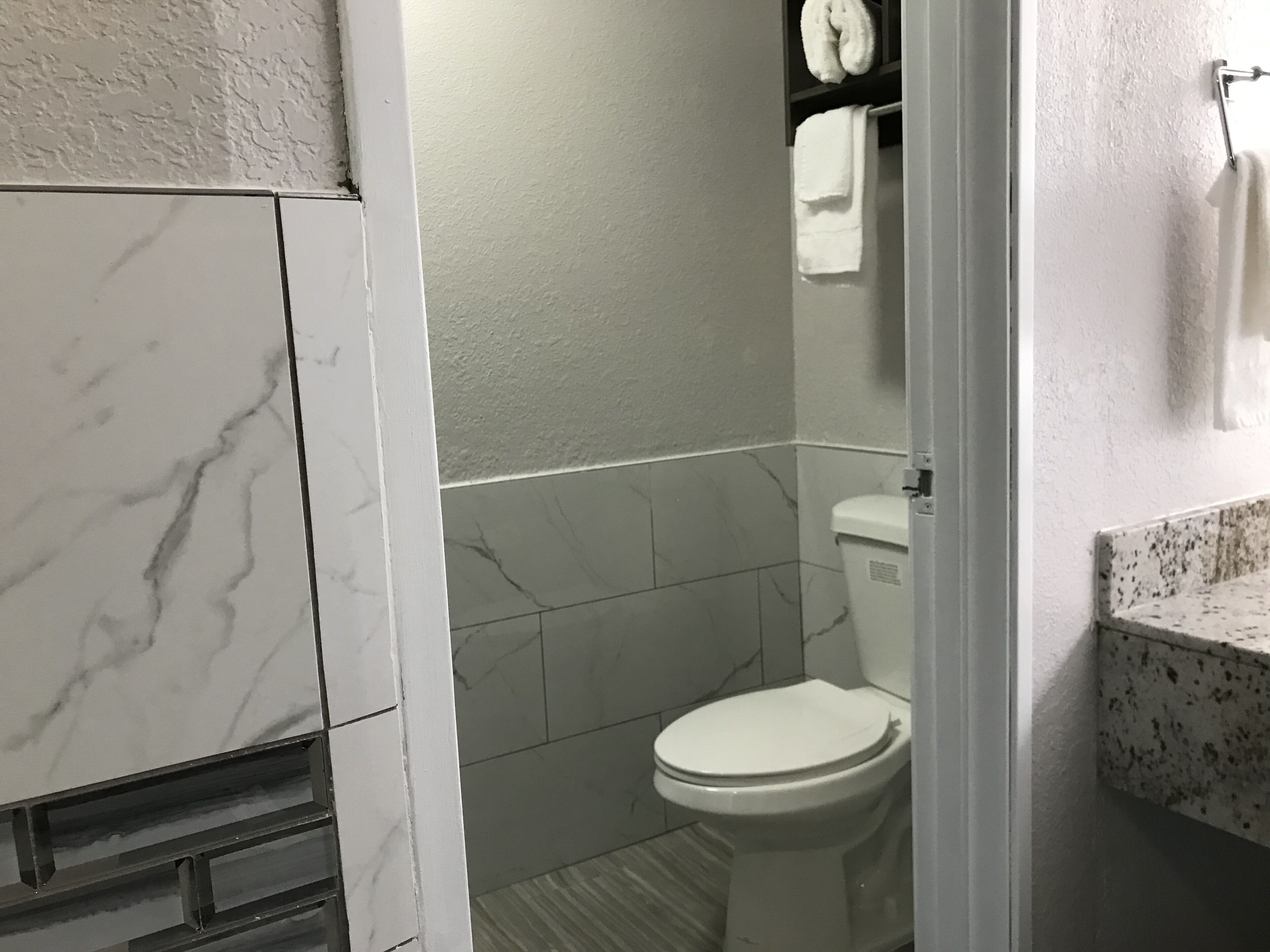 Une salle de bain avec des toilettes, des carreaux de marbre et un lavabo blanc doté d’un plan de toilette à motifs.