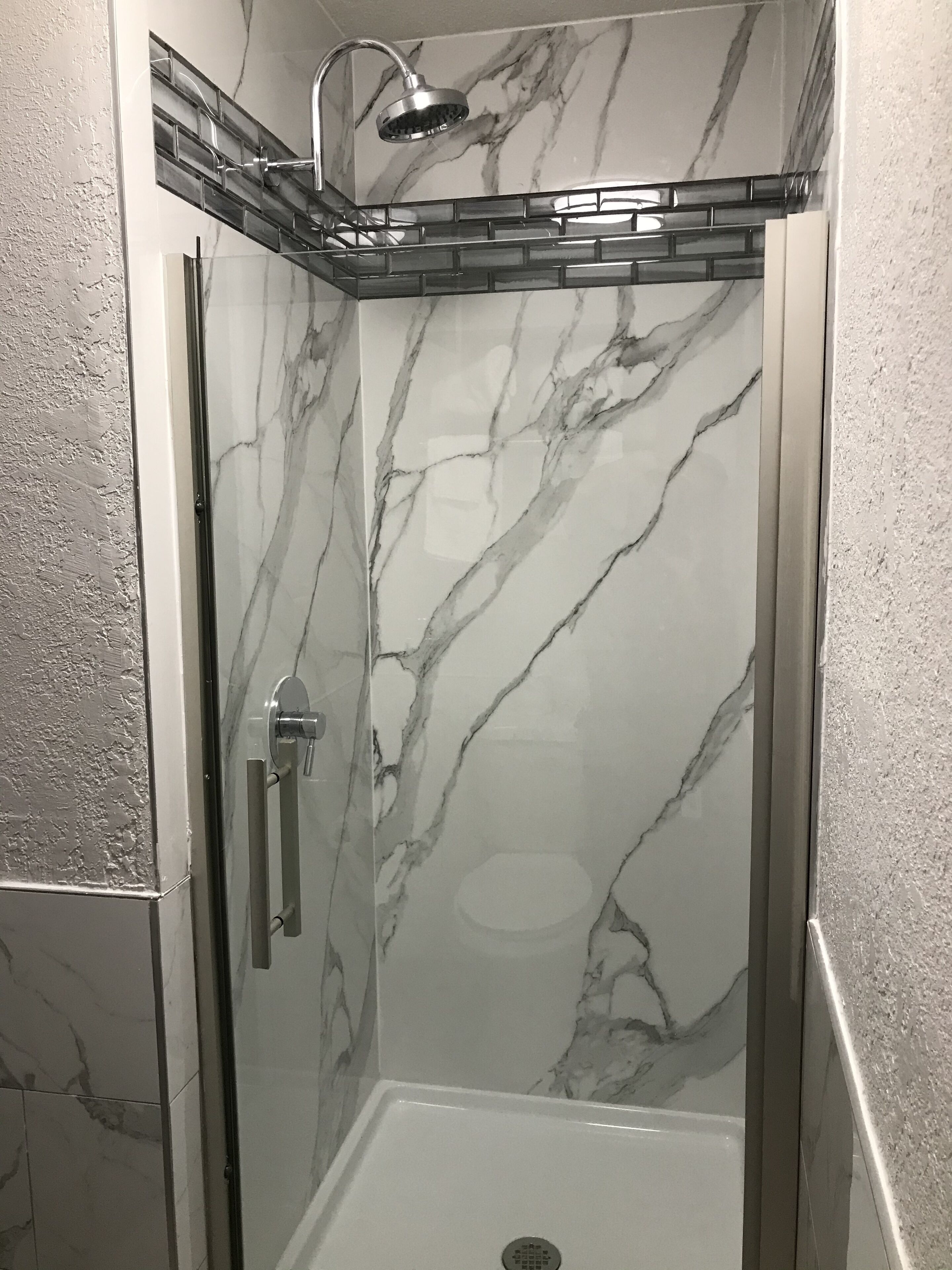 Ducha con cerramiento de vidrio, diseño de mármol, ducha y manija de vidrio.