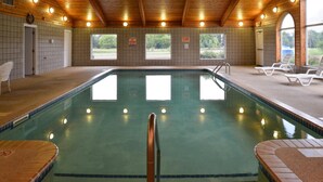 Una piscina interior con suelo de baldosas, techo de madera y vistas al exterior a través de ventanas.