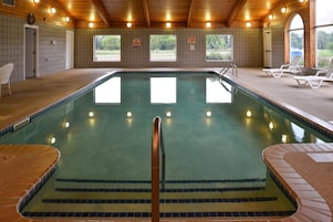 Una piscina interior con suelo de baldosas, techo de madera y vistas al exterior a través de ventanas.
