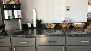Una zona de cocina con cafetera, vasos de papel y dispensadores de condimentos.