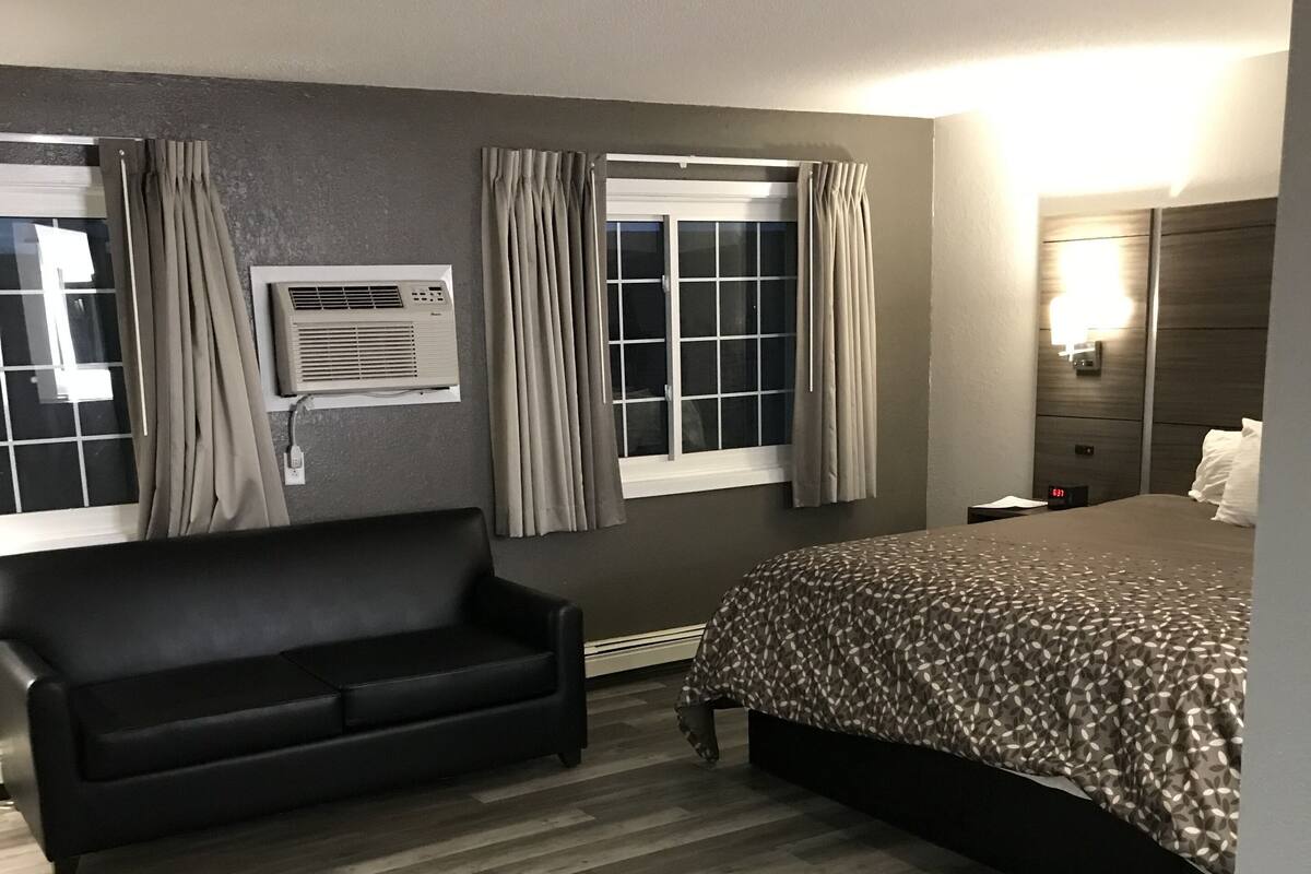 A hotel room with a bed, a sofa, a desk, and a window with curtains.