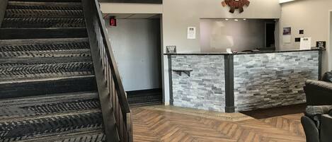 A reception area with a stone counter, a wooden staircase, and a herringbone-patterned floor.