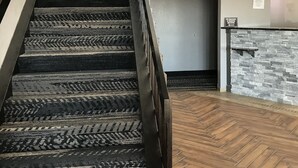 Una escalera con barandal de madera y alfombra estampada, que conduce a una habitación con pared de piedra y un letrero que indica una máquina de hielo.
