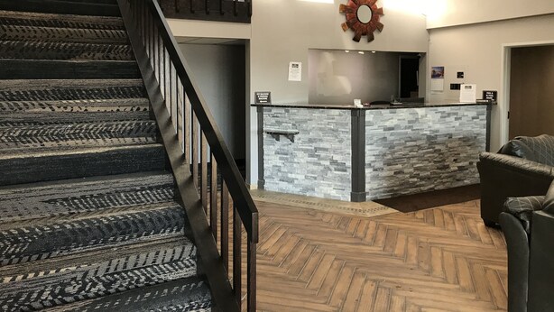 Un vestíbulo de hotel con una escalera de madera, una recepción con mostrador de piedra y un suelo con motivo de espiga.