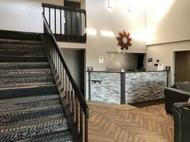 Un vestíbulo de hotel con una escalera de madera, una recepción con mostrador de piedra y un suelo con motivo de espiga.