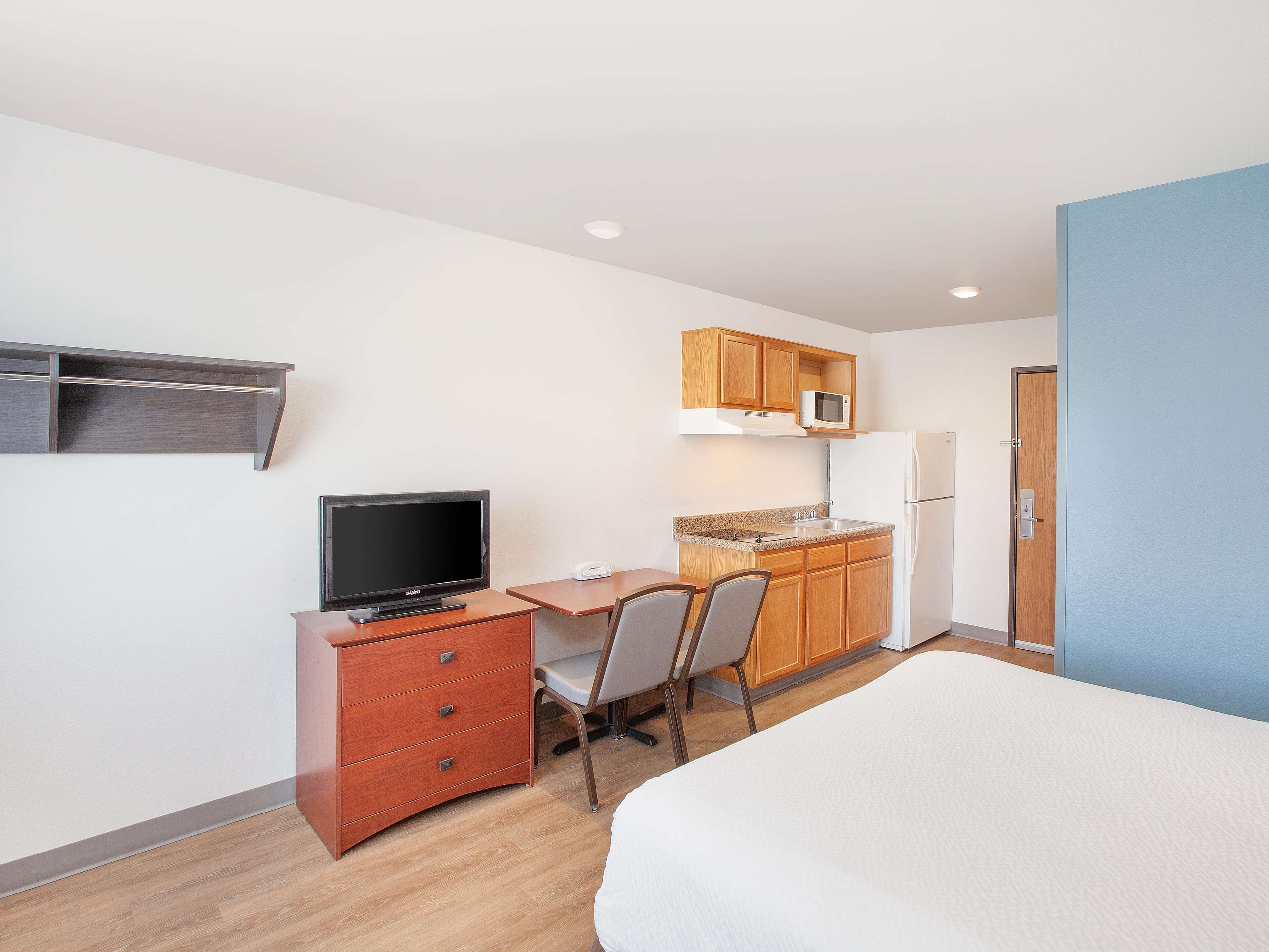 A compact hotel room with a bed, a desk with a chair, a television, a microwave, a refrigerator, and a wooden cabinet.